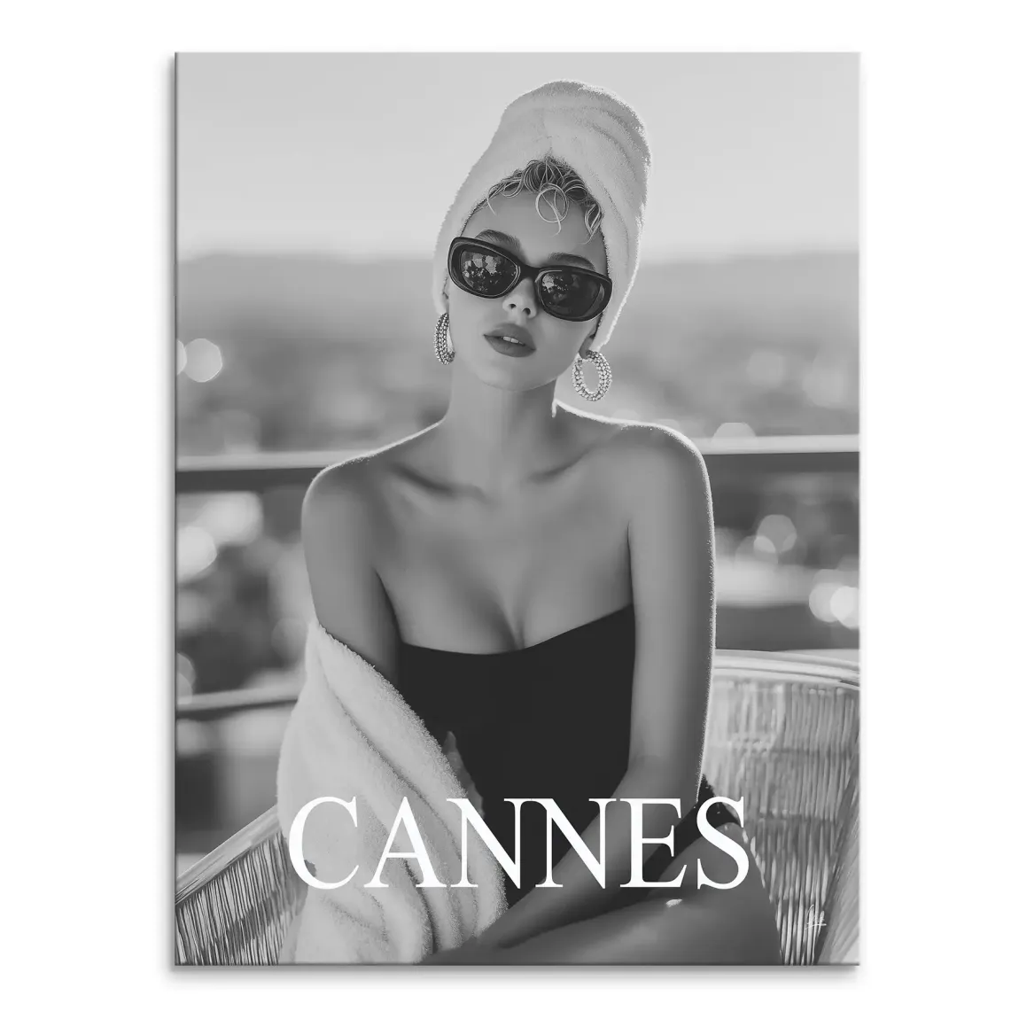 Black and white fashion portrait of a glamorous woman with a towel on her head, sunglasses, and a strapless top, with Cannes text overlay over a blurred outdoor backdrop.
