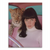 Stylish woman with dark bangs and white turtleneck in a vintage pink car interior beside a leopard.