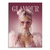 Portrait of a glamorous woman with pink hair styled in buns, heart-shaped pink sunglasses with rhinestones, and pearl and rhinestone jewelry, wearing a pink sequin top with a feather boa against a glam magazine-inspired backdrop.